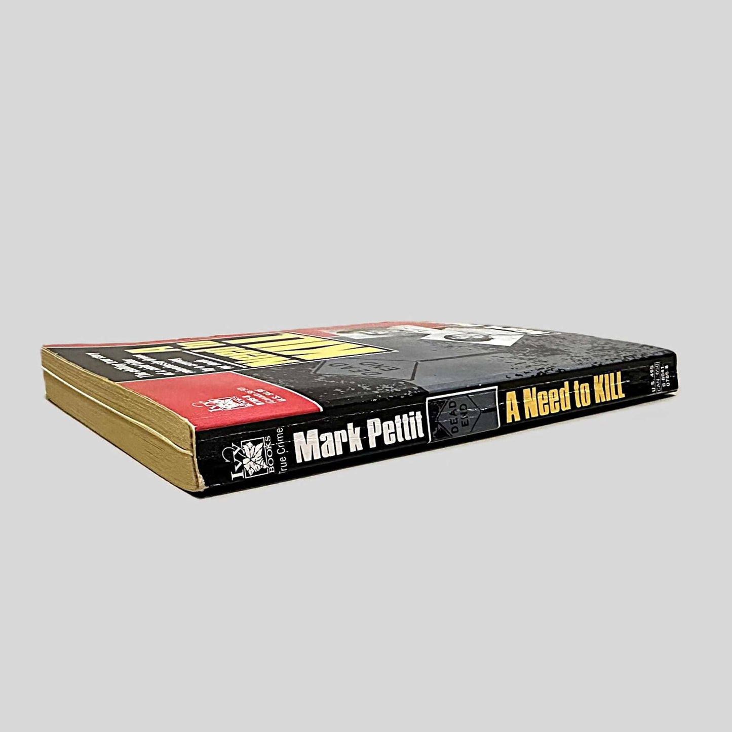 Close-up spine view of A Need to Kill by Mark Pettit centered on a neutral light gray background. Spine shows creasing and bumping.