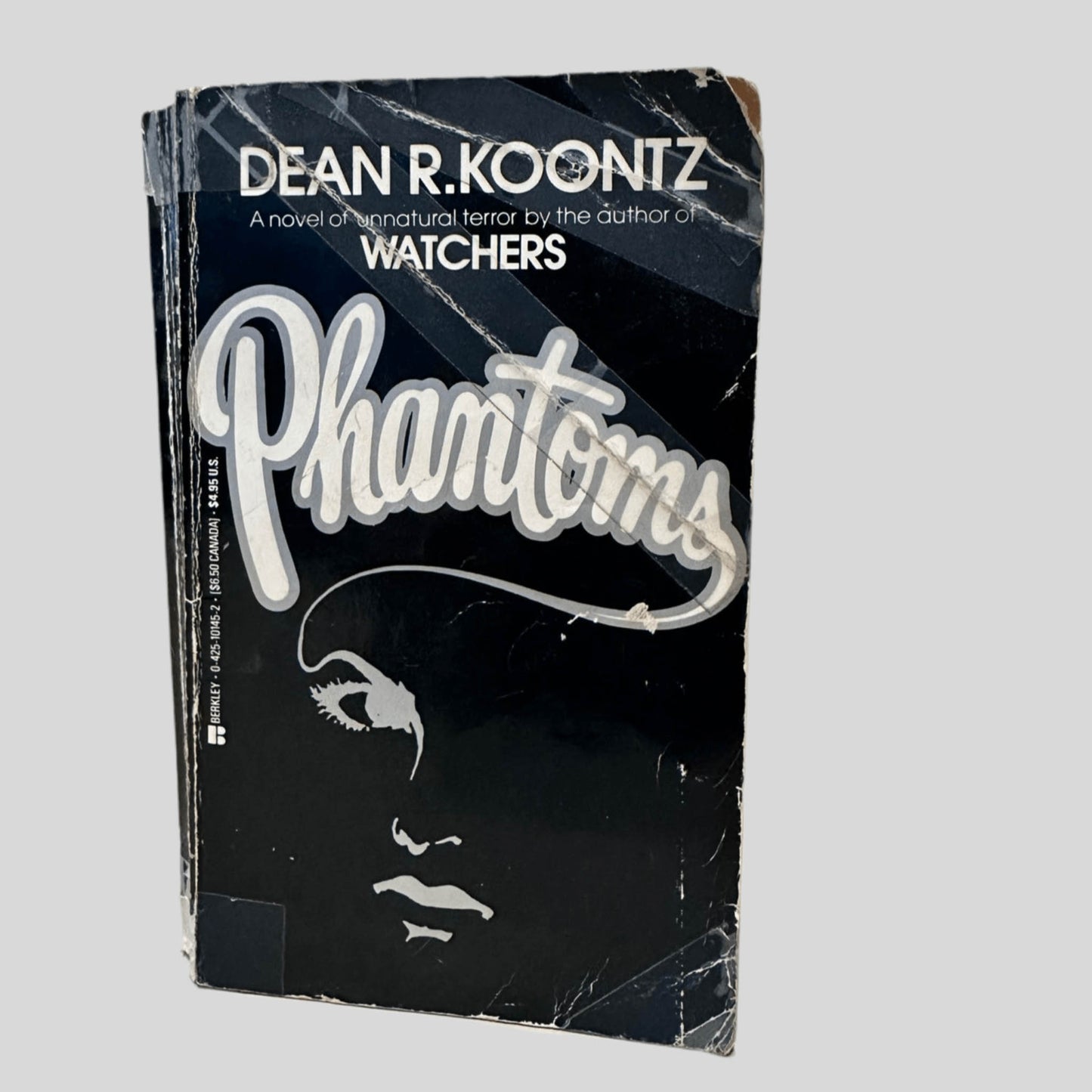 Front cover view of Front cover view of Phantoms by Dean R. Koontz centered on a neutral light gray background. Extensive creasing and chipping to the front cover. Transparent tape is preventing the creases from detaching from the book cover entirely. centered on a neutral light gray background.