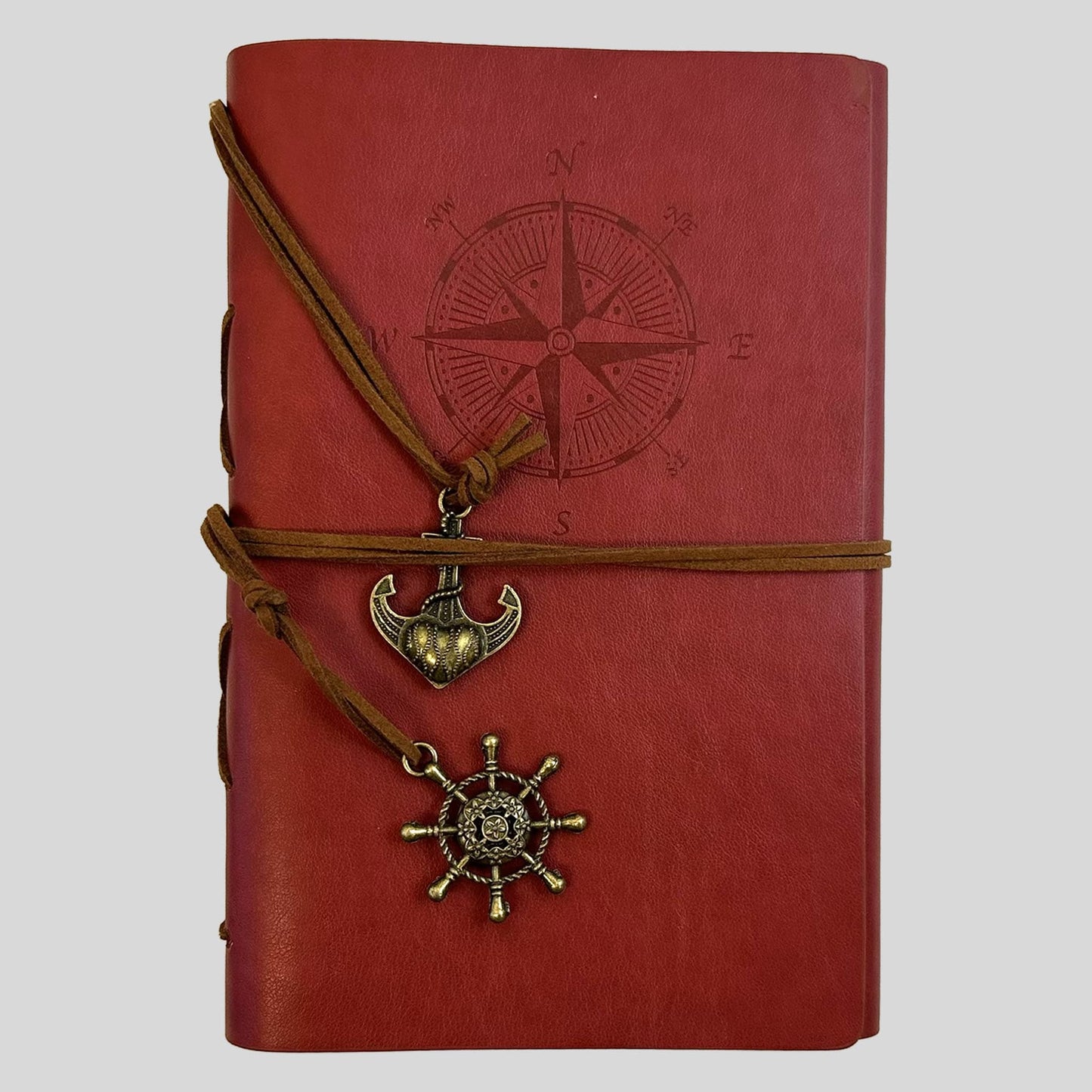 A professional product shot of a vibrant red faux-leather journal from the Fehmerling Books standalone collection. The screen showcases an embossed compass rose on the cover, wrapped in brown twine and accented with antique gold-toned anchor and ship wheel charms. This high-quality image captures a bold and adventurous aesthetic, perfect for creative writing and documenting travels.