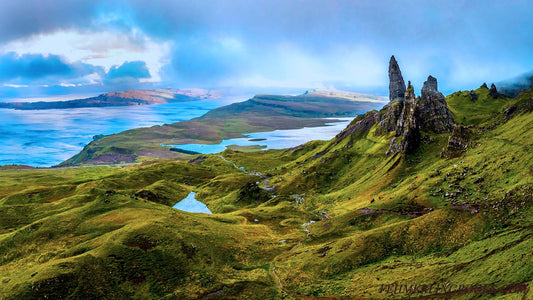 Lush green highlands with a view of the sky and water below.