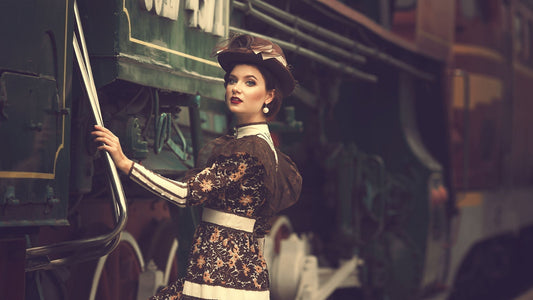 Woman in vintage attire standing next to a green train.