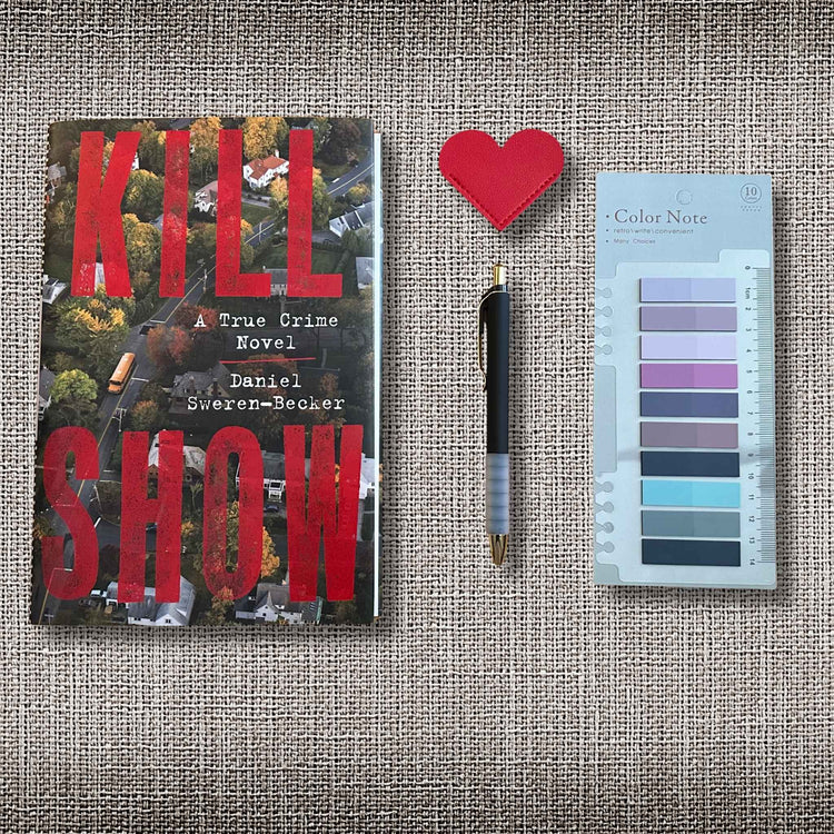 Flatlay image of a hardcover book, a pen, a heart shaped leather bookmark, and annotation tabs on a grey linen background