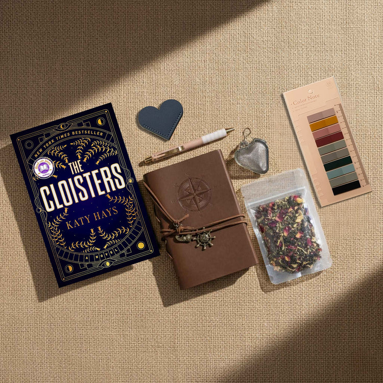 Flatlay image of a book, journal, heart shaped leather bookmark, a pen, a heart shaped tea infuser, loose leaf tea, and annotation tabs on a linen background.