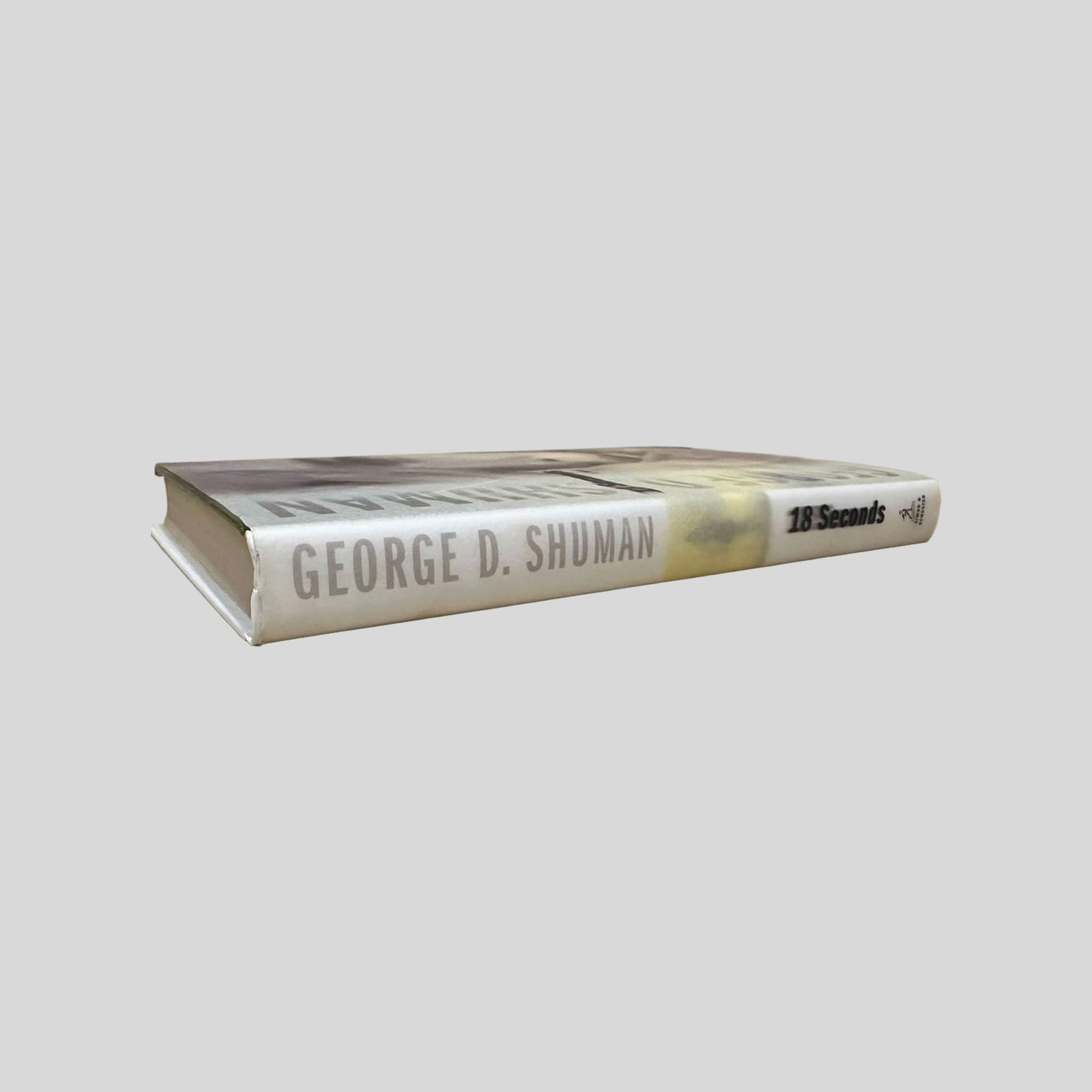 Spine of the 18 Seconds hardcover by George Shuman. Displays the author’s name and title in beige lettering against a white background. The visual confirms the book's Very Good condition with a tight, well-preserved binding.
