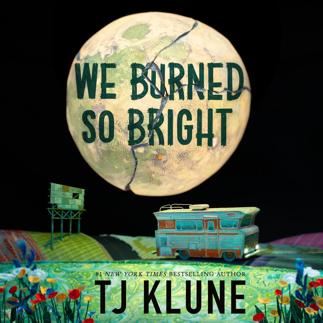 A large, cracked, parchment-textured moon hangs in a black sky with the title 'We Burned So Bright' written across it in dark teal. Below, a miniature teal and orange RV sits in a vibrant, patchwork-quilt landscape filled with tiny red and blue wildflowers. The author’s name, TJ Klune, is prominently displayed at the bottom.
