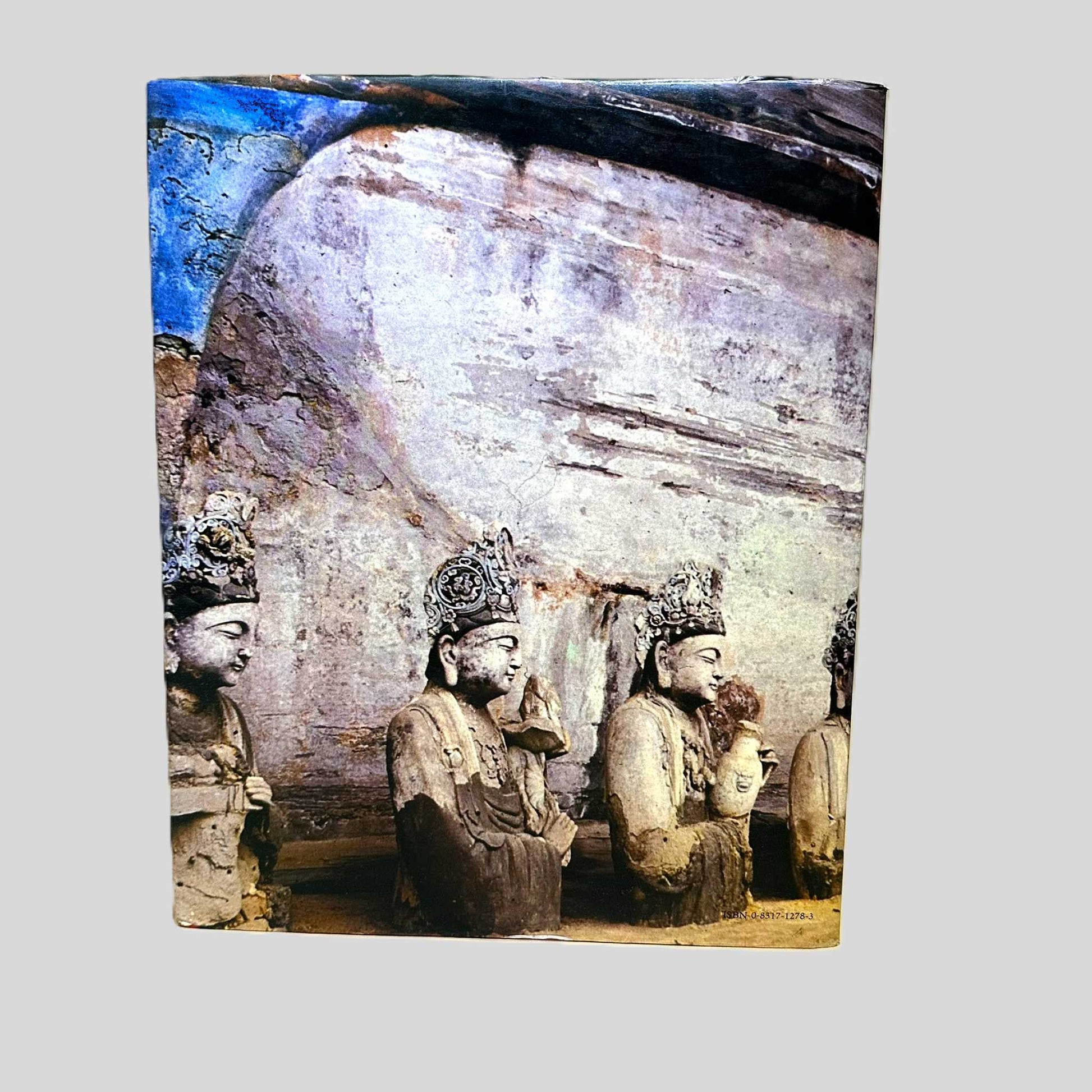 The back cover of the oversized 1980 edition of 'China' by Zheng Shifeng and others. The full-bleed photographic cover depicts an ancient Buddhist rock-cut grotto with weathered stone statues of seated figures carved into a cliffside. The image captures the authentic vintage aging and monumental scale of Chinese cultural heritage sites like the Longmen or Yungang Grottoes.