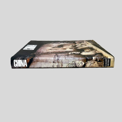 Side-angle view of the oversized volume 'China' resting on a grey surface. The screen captures the bold title and Gallery Books branding on the spine, reflecting the high-quality production of the late 20th century. The layout emphasizes the artistic and cultural significance of the Buddhist imagery featured on the dust jacket.