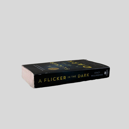 Close-up spine view of A Flicker in the Dark by Stacy Willingham centered on a neutral light gray background. Spine shows minimal creasing and chipping at the top of the spine.