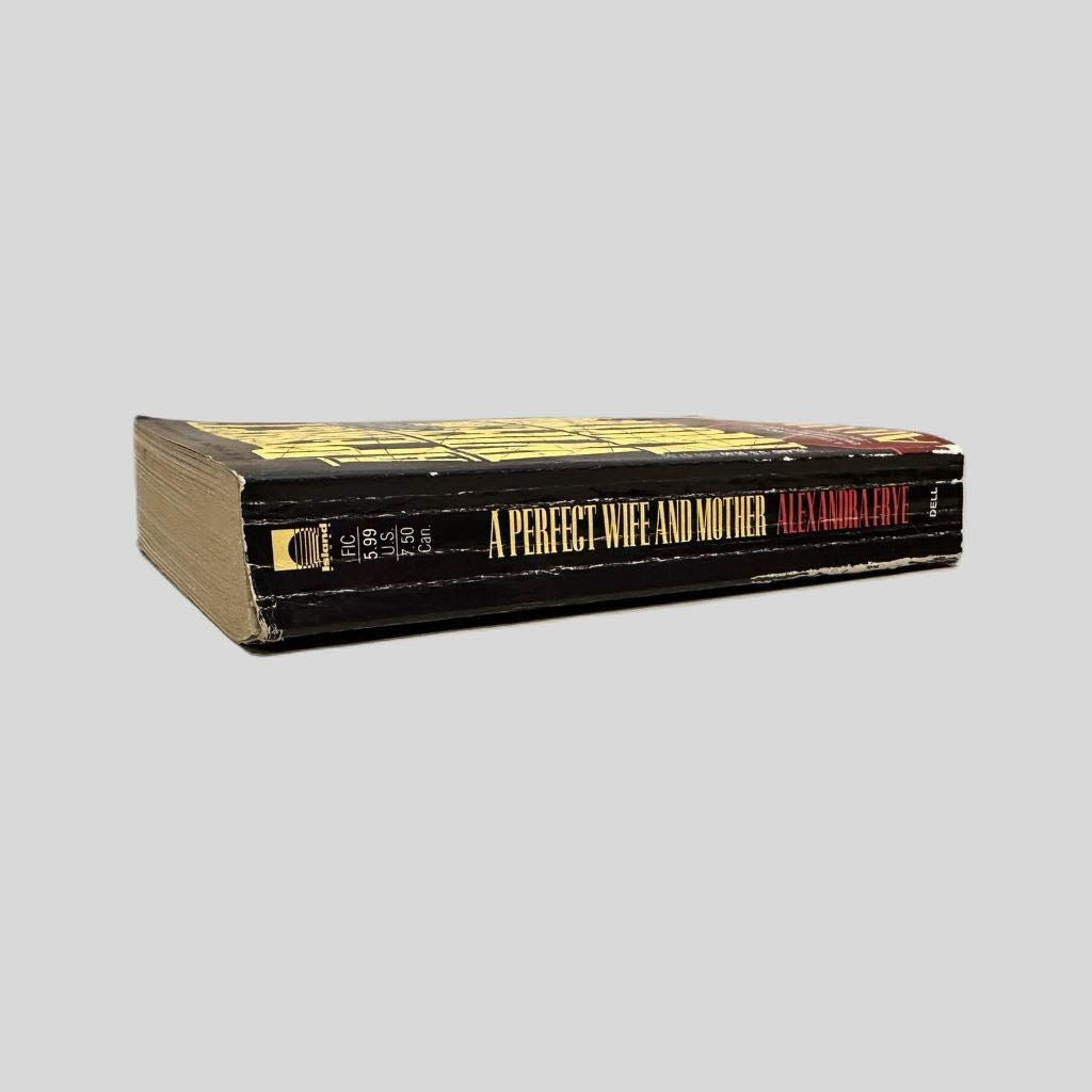 Close-up spine view of A Perfect Wife and Mother by Alexandra Frye centered on a neutral light gray background. Spine shows creasing. Chipping is present along the lower back half of the spine. Pages lay flat.