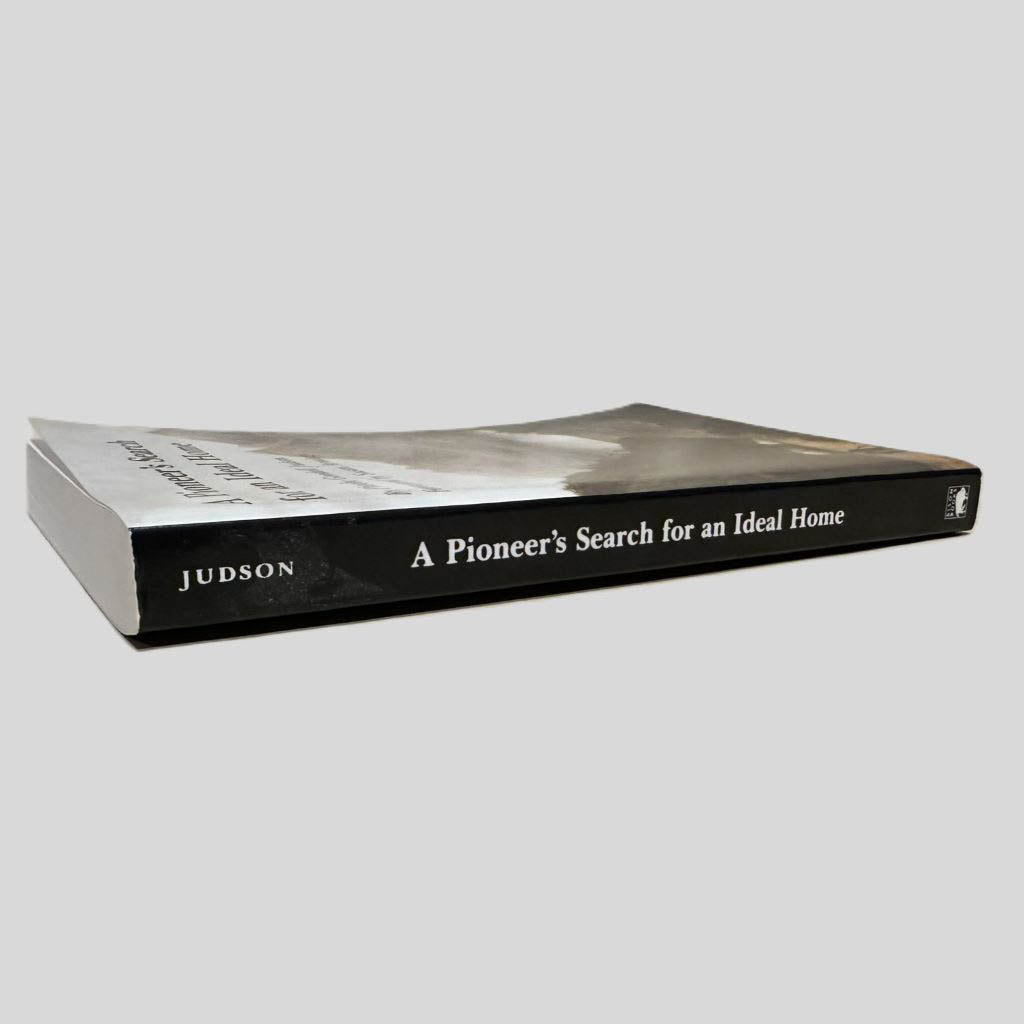 Close-up spine view of A Pioneer's Search for an Ideal Home by Phoebe Goodell Judson centered on a neutral light gray background. Spine is square and shows no creasing. Pages lay flat.
