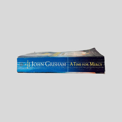 Close-up spine view of A Time for Mercy by John Grisham centered on a neutral light gray background. Spine shows creasing. Pages lay flat.