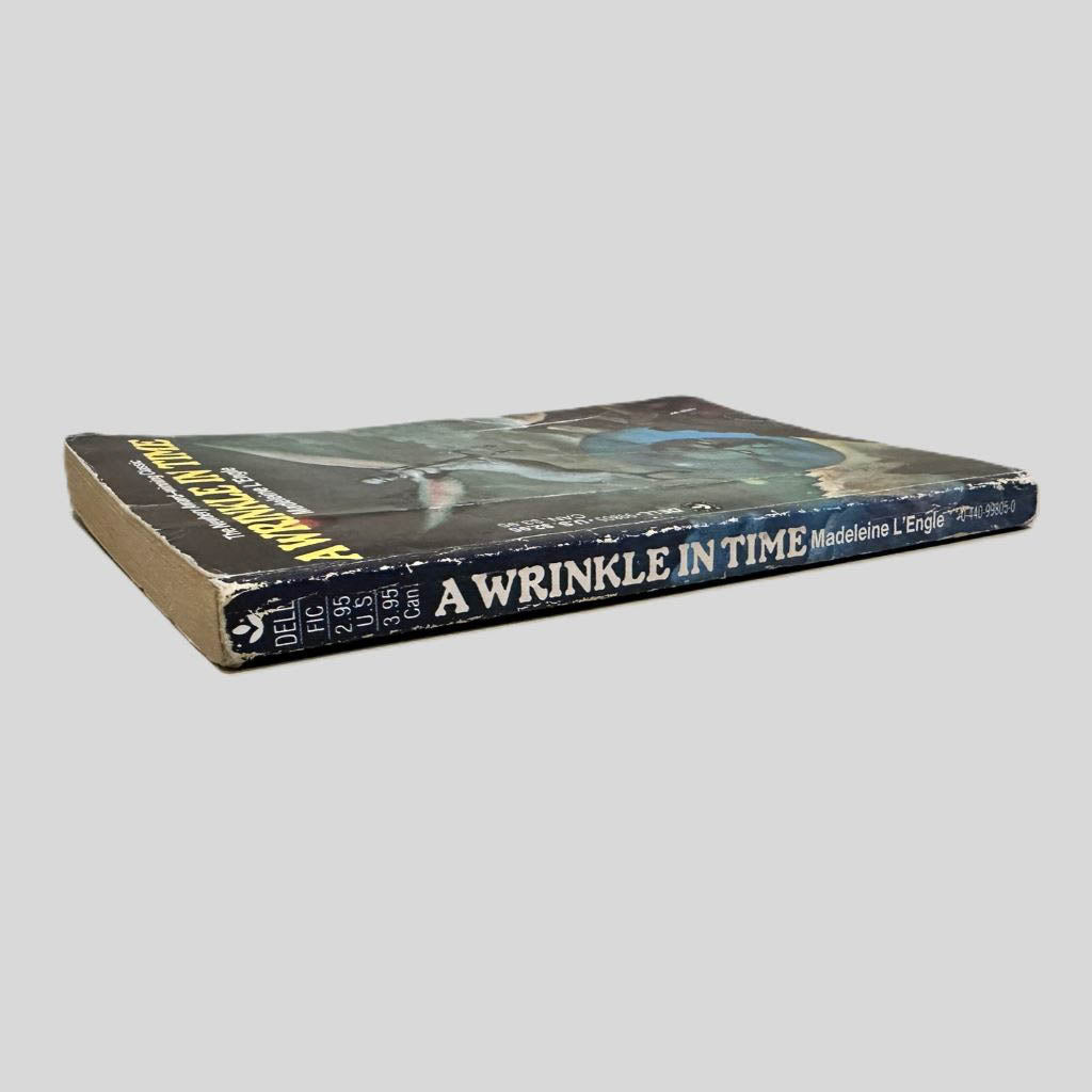 Close-up spine view of A Wrinkle in Time by Madeleine L'Engle centered on a neutral light gray background. Spine shows creasing and chipping. Spine is square and pages lay flat.