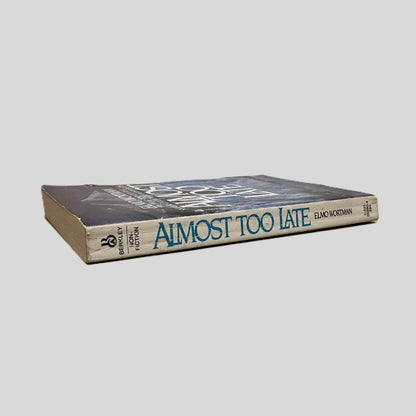 Close-up spine view of Almost Too Late by Elmo Wortman centered on a neutral light gray background. Spine shows minor chipping at the top and minimal creasing. Pages lay flat.