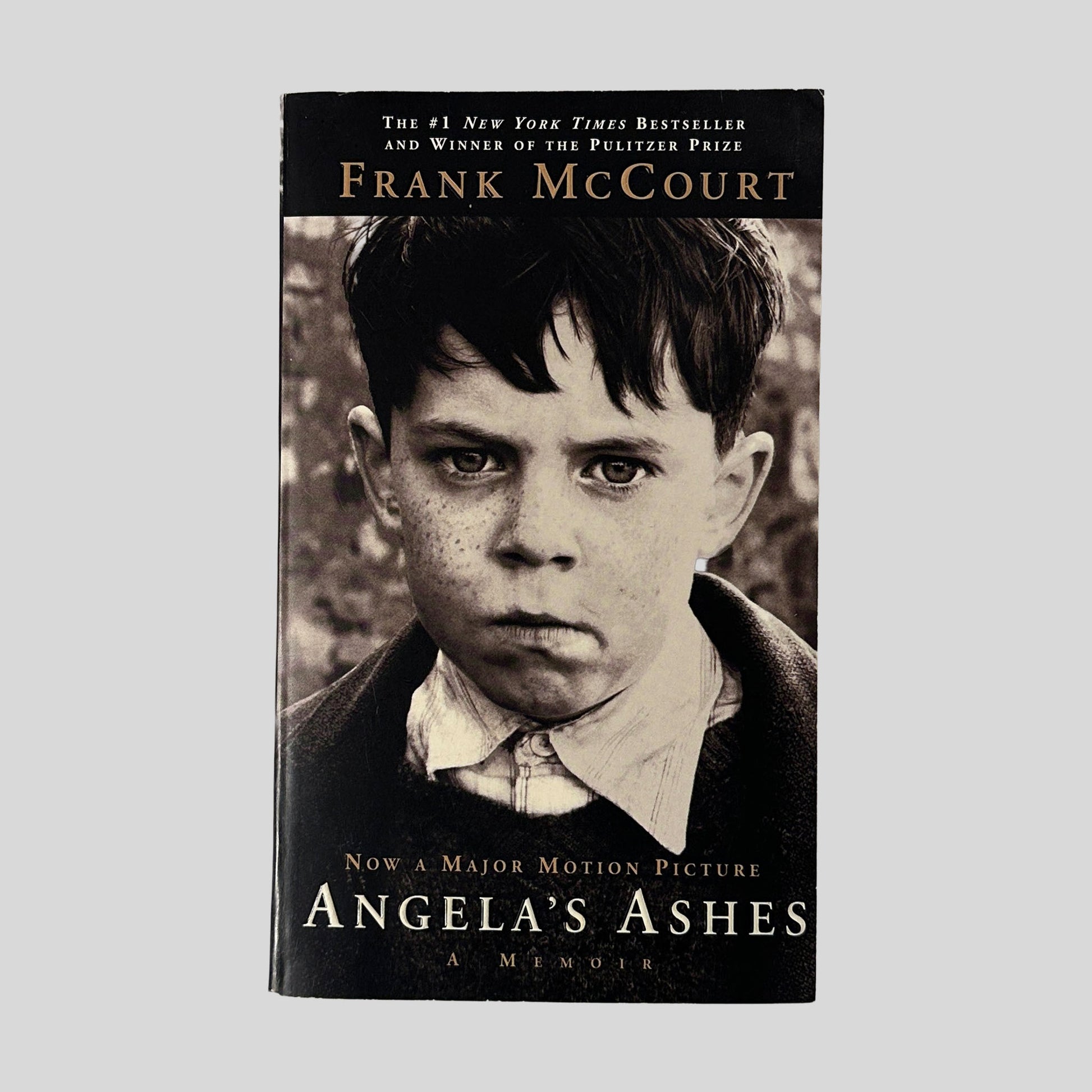 The front cover of "Angela's Ashes" by Frank McCourt, featuring a sepia-toned close-up photograph of a serious, freckled young boy.