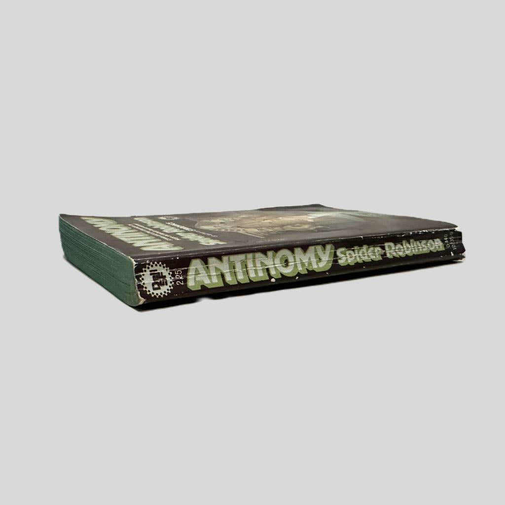 Close-up spine view of Antinomy by Spider Robinson centered on a neutral light gray background. Spine shows creasing; chipping to the top and bottom of spine. Pages lay flat.