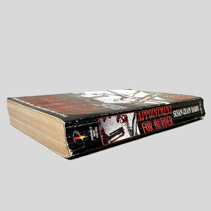 Close-up spine view of Appointment For Murder by Susan Crain Bakos centered on a neutral light gray background. Spine shows creasing and rubbing.