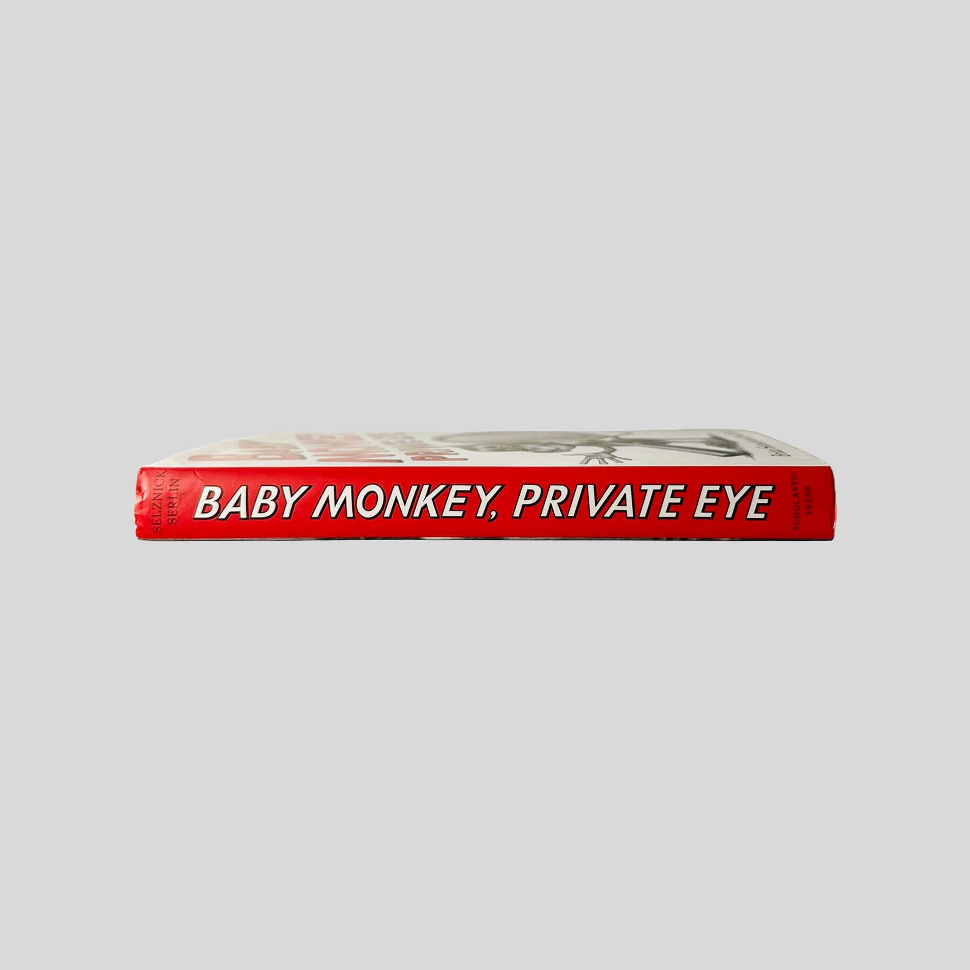 Close-up spine view of Baby Monkey, Private Eye by Brian Selznick & David Serlin centered on a neutral light gray background. Dust jacket is present and shows no damage. Spine shows no creasing. Pages lay flat.