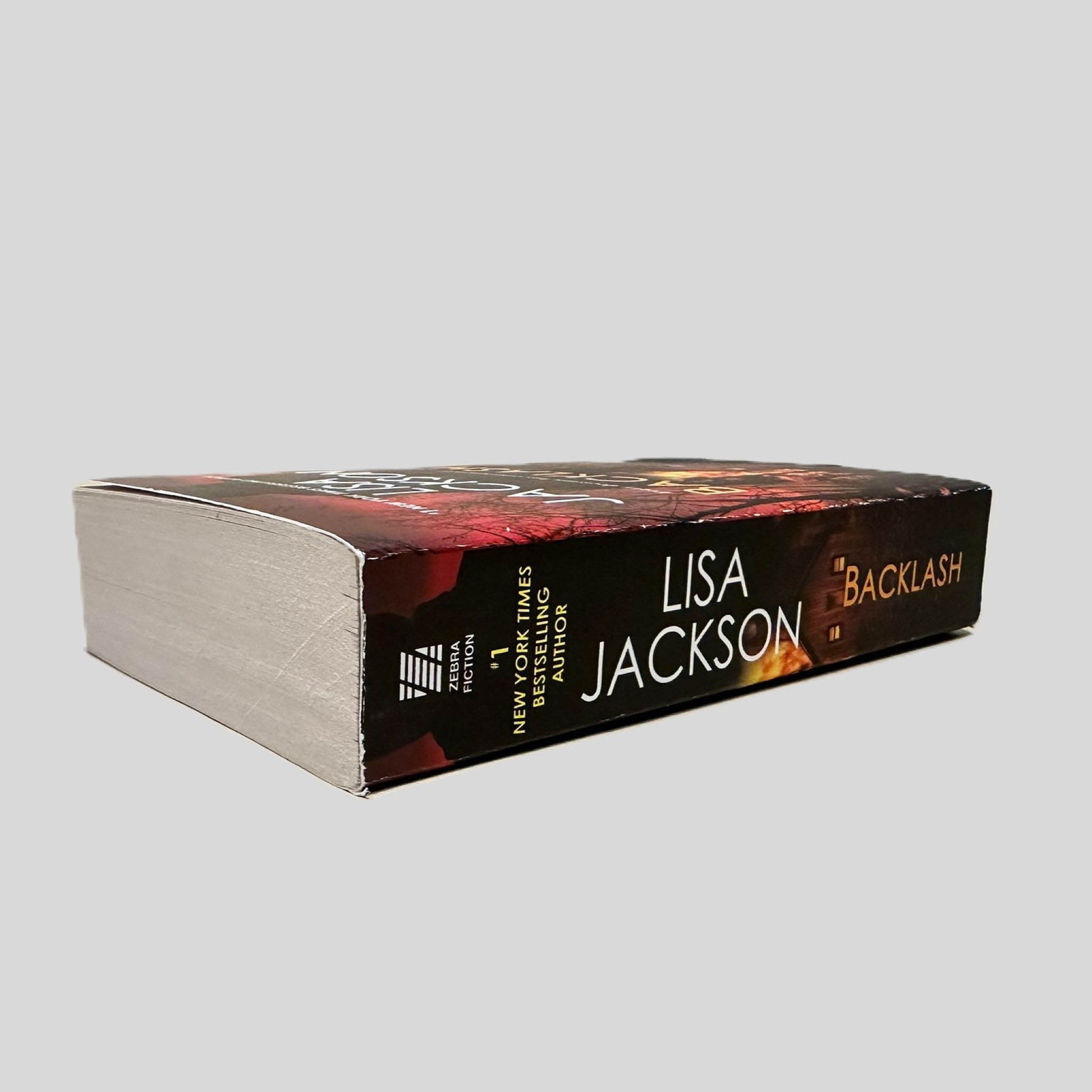Close-up spine view of Backlash by Lisa Jackson centered on a neutral light gray background. Spine is square and shows no creasing.