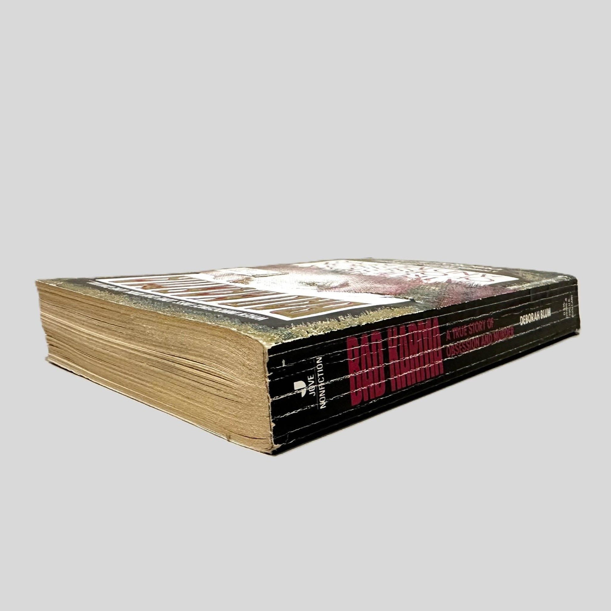 Close-up spine view of Bad Karma by Deborah Blum centered on a neutral light gray background. Spine shows creasing and rubbing.