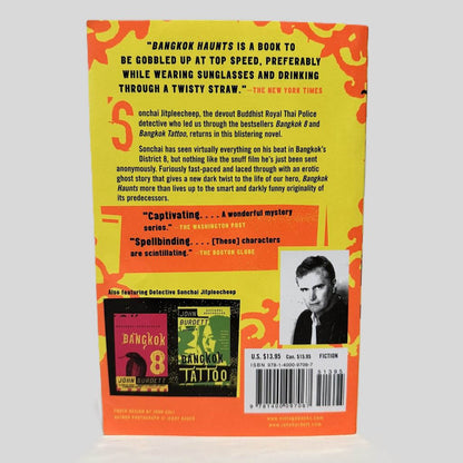 Back cover view of Bangkok Haunts by John Burdett centered on a neutral light gray background. Chipping along the top edge.