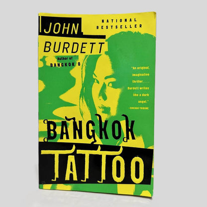 Front cover view of Bangkok Tattoo by John Burdett centered on a neutral light gray background. Chipping on the corners.