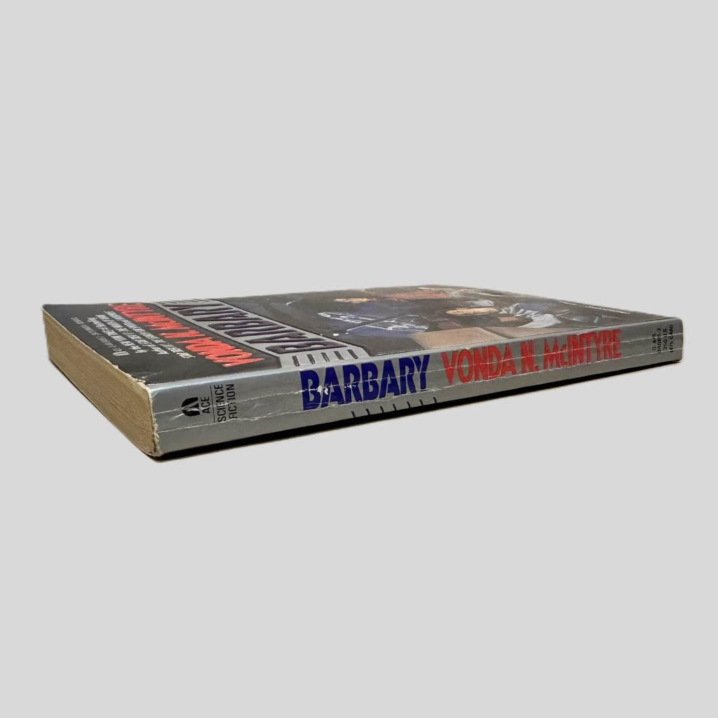 Close-up spine view of  centered on a neutral light gray background. Spine shows creasing. Pages lay flat.