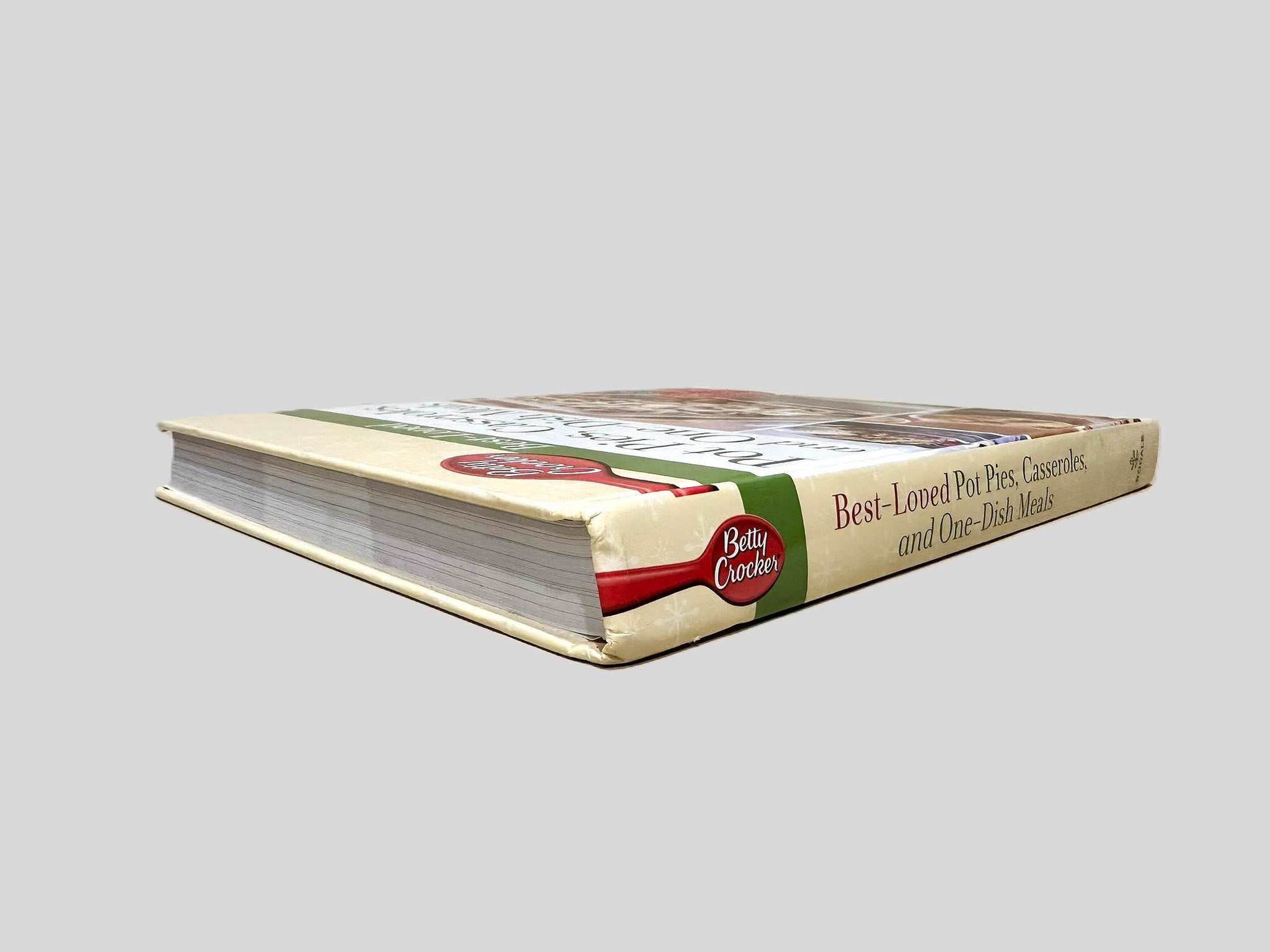 Close-up spine view of Betty Crocker Best-Loved Pot Pies, Casseroles, and One-Dish Meals centered on a neutral light gray background. Spine shows bumping at the top of the spine and no creasing. Pages lay flat.