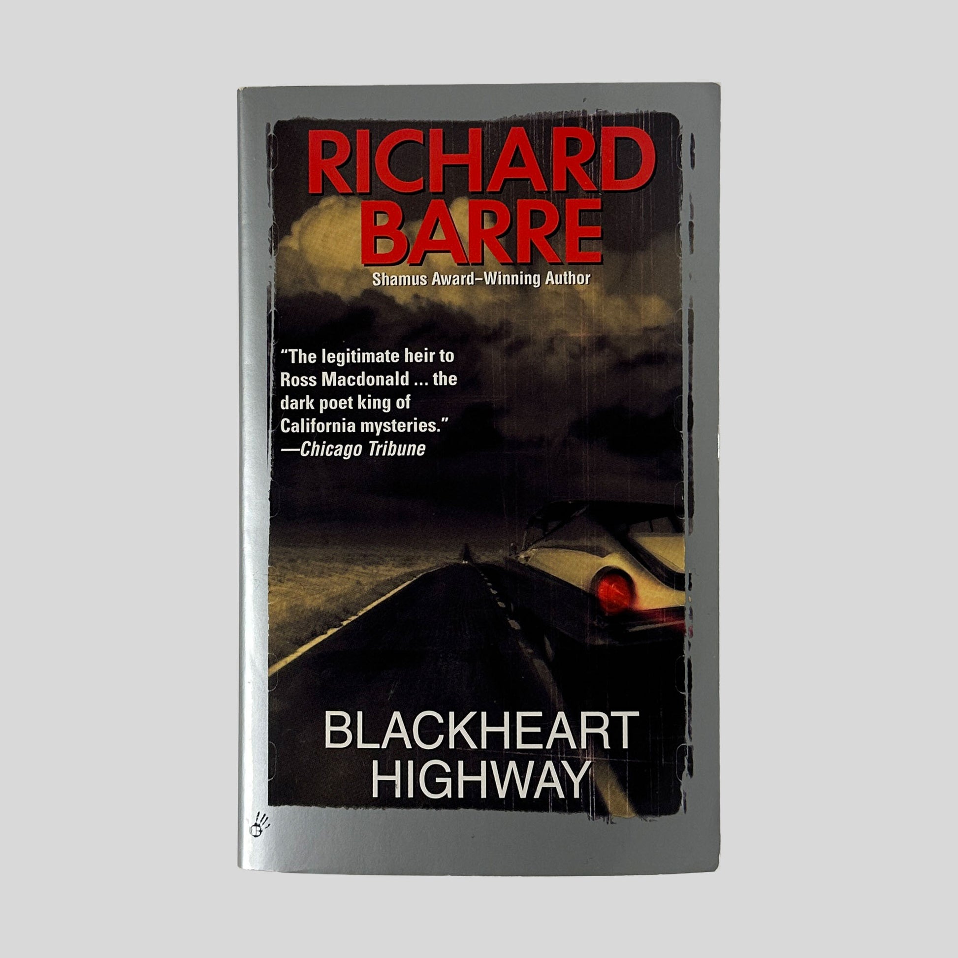 The front cover of the paperback Blackheart Highway by Richard Barre, featuring a dark photograph of a road at night with the glowing red taillights of a car in the distance.