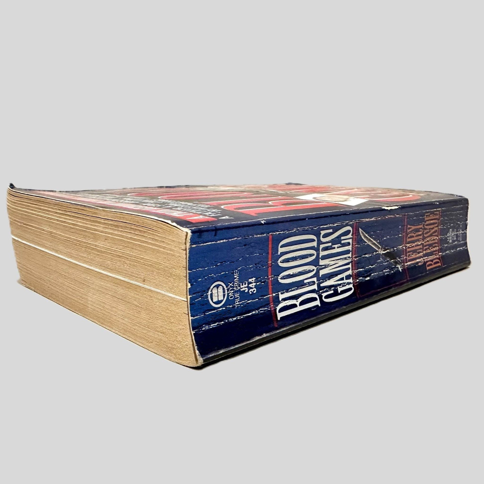 Close-up spine view of Blood Games by Jerry Bledsoe centered on a neutral light gray background. Spine shows creasing and rubbing.