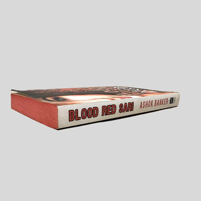 Close-up spine view of Blood Red Sari by Ashok Banker centered on a neutral light gray background. Spine is square and shows no visible creasing.