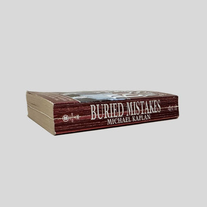Close-up spine view of Buried Mistakes by Michael Kaplan centered on a neutral light gray background. Spine shows creasing and rubbing.
