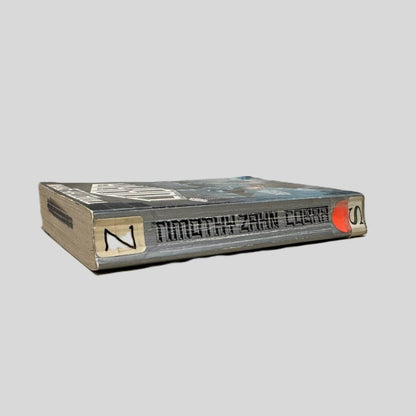 Close-up spine view of COBRA by Timothy Zahn centered on a neutral light gray background. Spine shows creasing. Library shelving stickers are taped to the top and bottom ends of the spine. Pages lay flat.