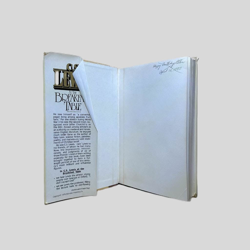 Inside front cover view of C.S. Lewis At the Breakfast Table Edited by James T. Como centered on a neutral light gray background. Dust jacket is present. Inside corner of the jacket is folded on top of itself. "Happy Birthday Ellen...April 16, 1980" is written in black ink in the top right cover page with an "X" over it in black ink.
