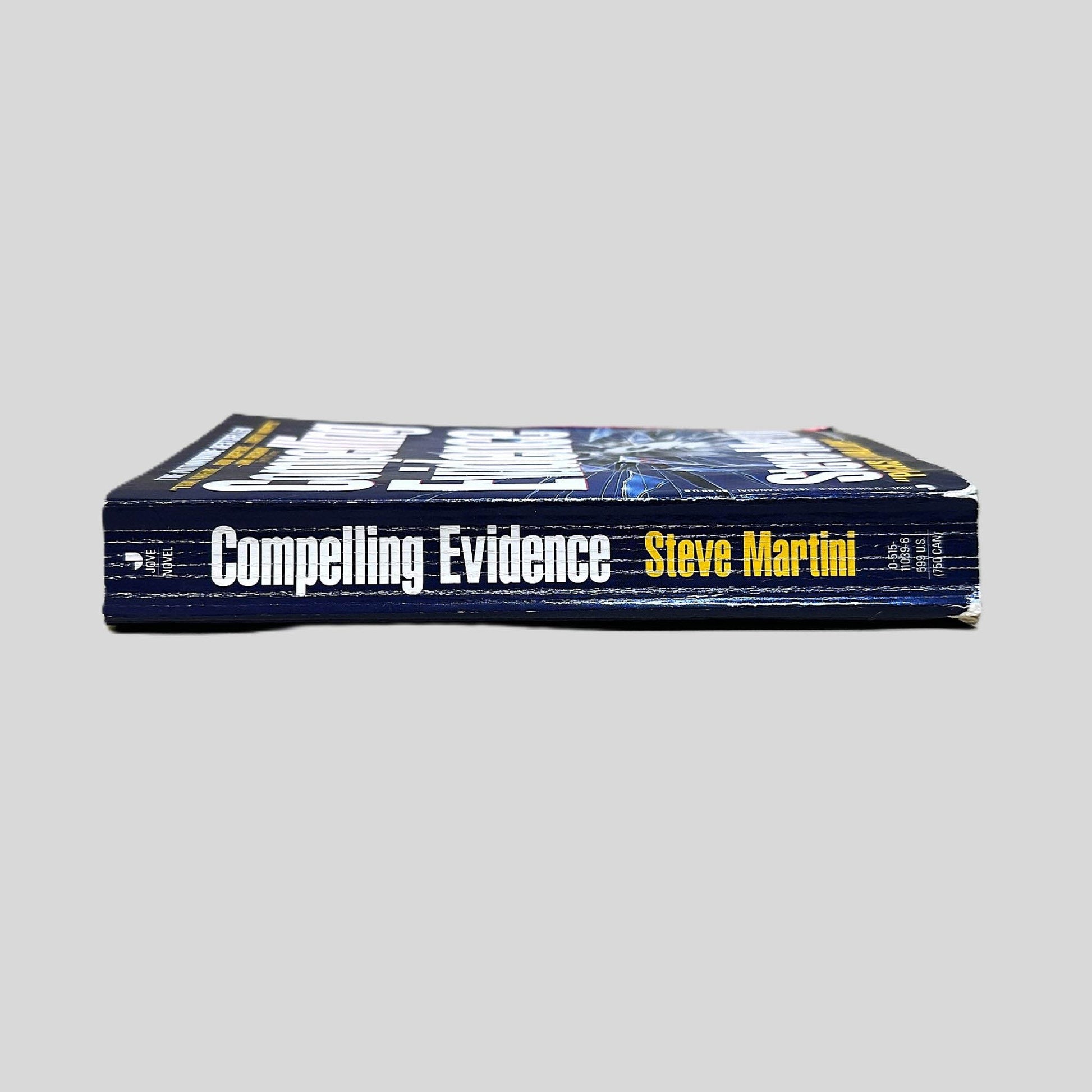 Close-up spine view of Compelling Evidence by Steve Martini centered on a neutral light gray background. Spine shows creasing.