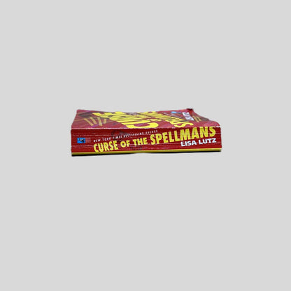 Close-up spine view of Curse of the Spellmans by Lisa Lutz centered on a neutral light gray background. Spine shows creasing and cocking. Pages lay flat.