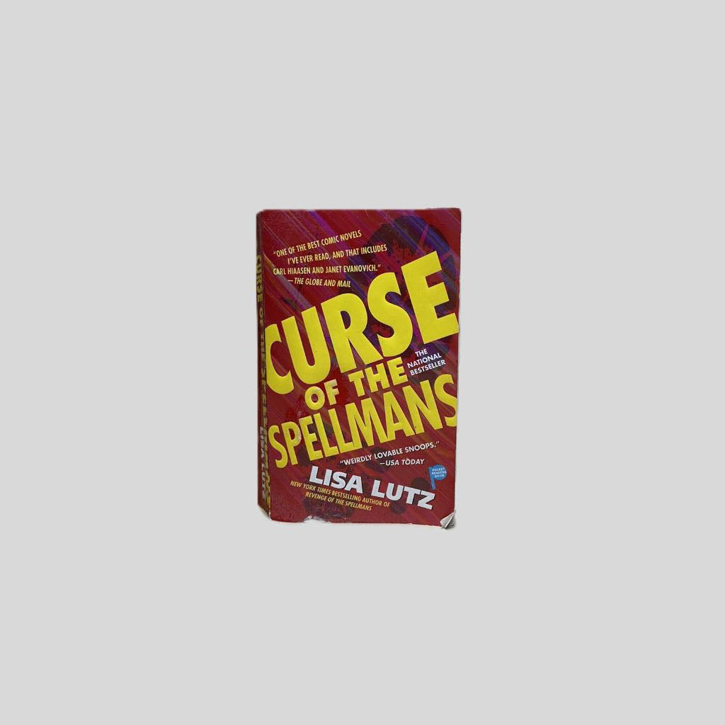 Front cover view of Curse of the Spellmans by Lisa Lutz centered on a neutral light gray background. Chipping and creasing around the edges and corners of the front cover.