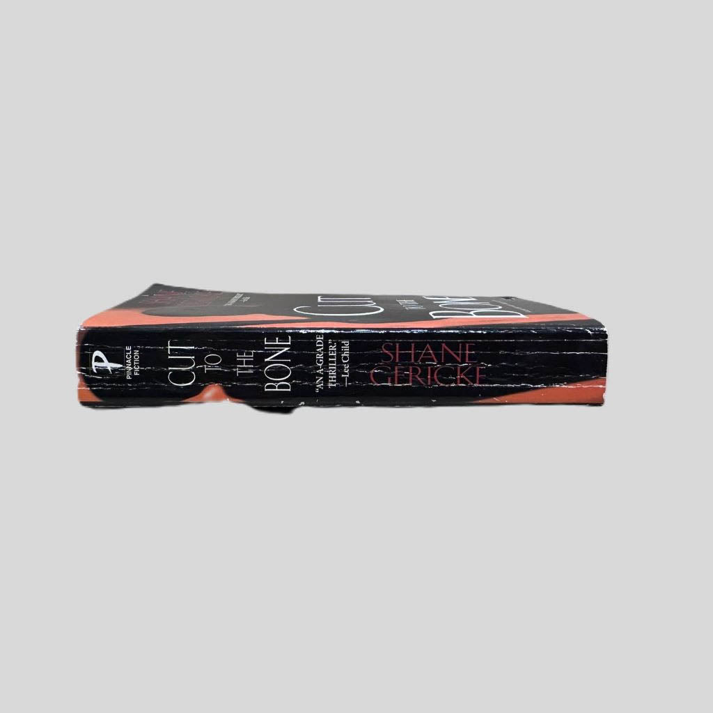Close-up spine view of Cut to the Bone by Shane Gericke centered on a neutral light gray background. Spine shows creasing.