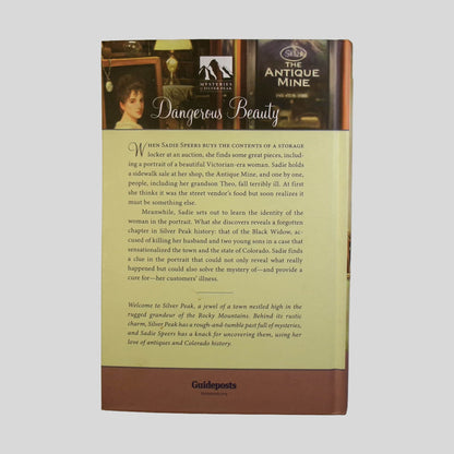 Back cover view of Dangerous Beauty by Carol Jefferson centered on a neutral light gray background. Cover does not lay flat - pages have water damage causing a wave. 