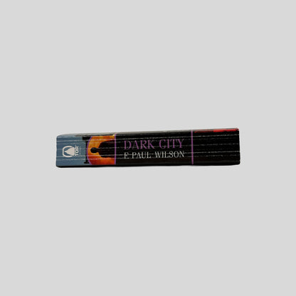 Close-up spine view of Dark City by F Paul Wilson centered on a neutral light gray background. Spine shows creasing. Pages lay flat.