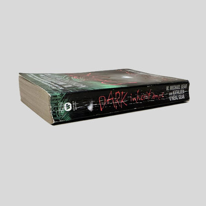 Close-up spine view of Dark Inheritance by W. Michael Gear & Kathleen O'Neal Gear centered on a neutral light gray background. Spine shows creasing. Pages lay flat.