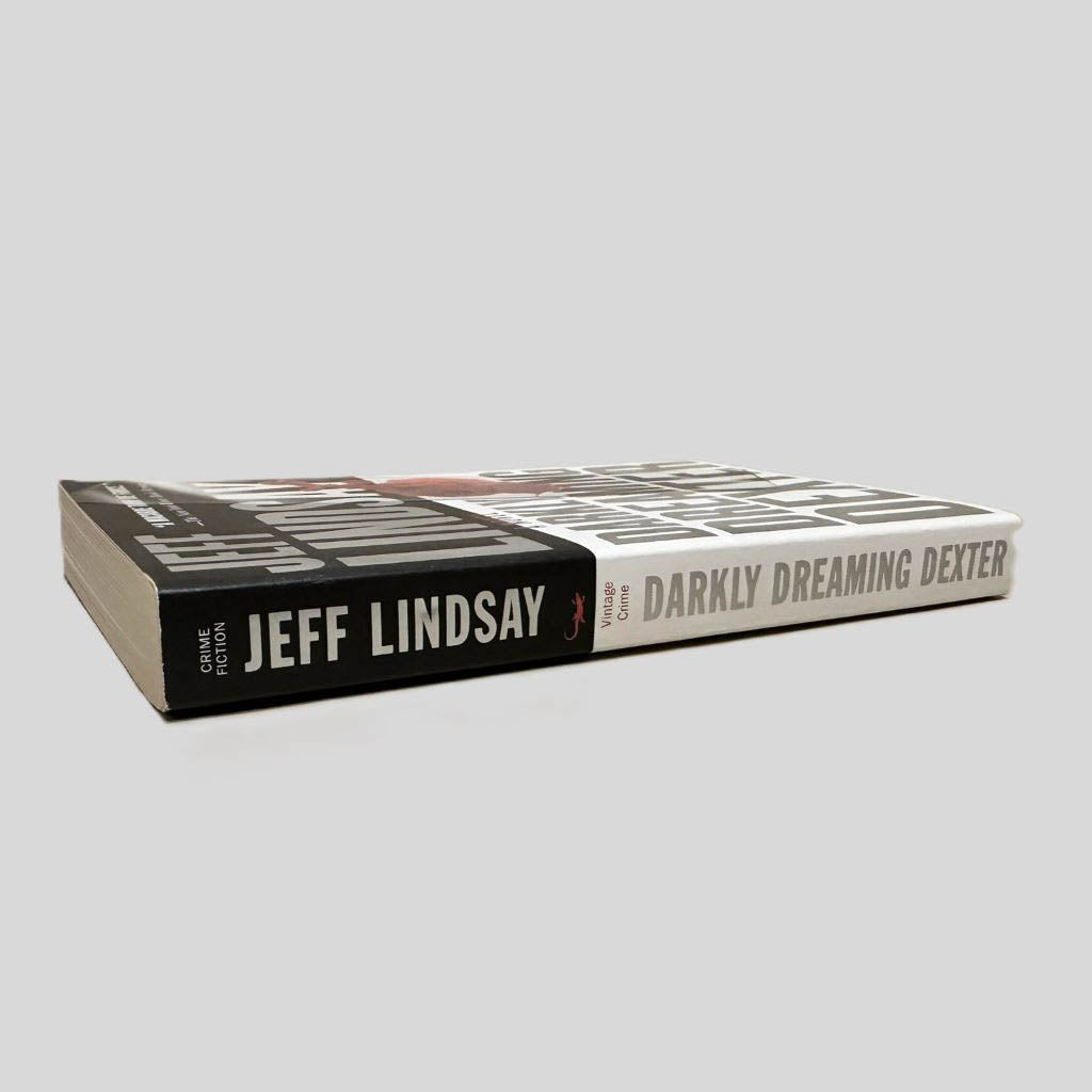 Close-up spine view of Darkly Dreaming Dexter by Jeff Lindsay centered on a neutral light gray background. Spine is square and shows no creasing.
