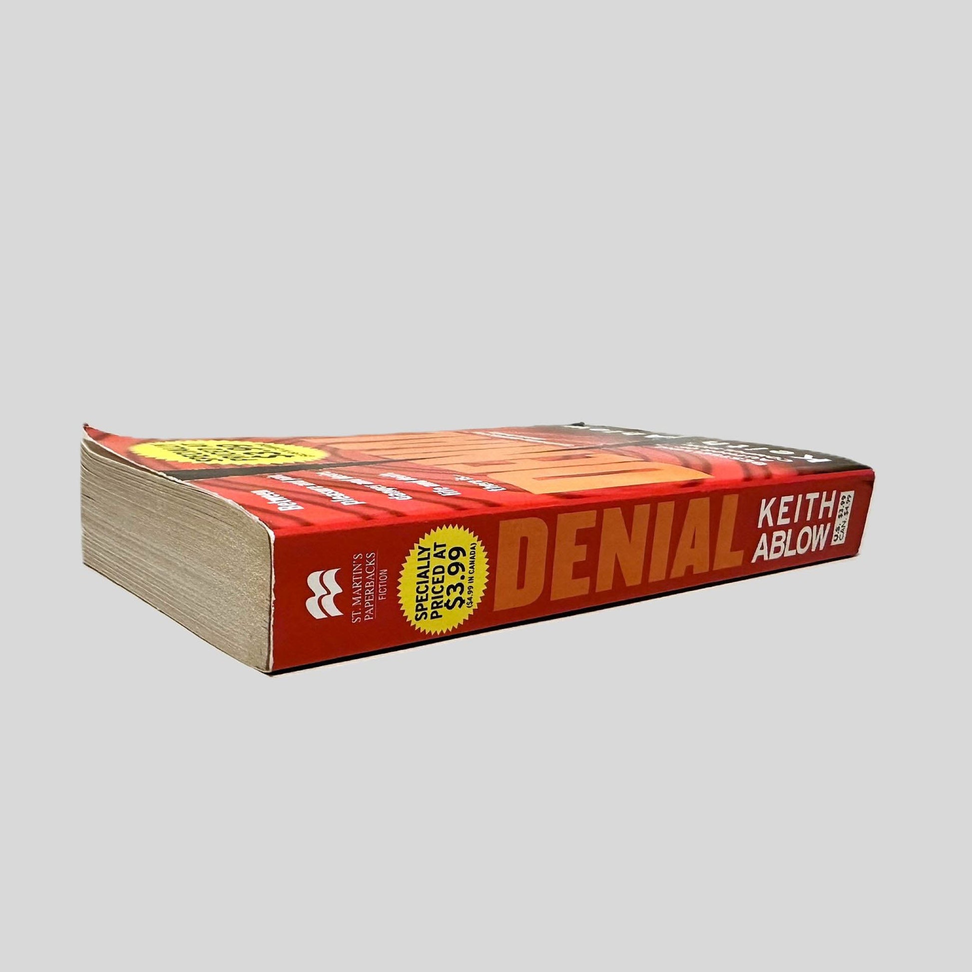 Close-up spine view of Denial by Keith Ablow centered on a neutral light gray background. Spine is square and shows no creasing. Pages lay flat.