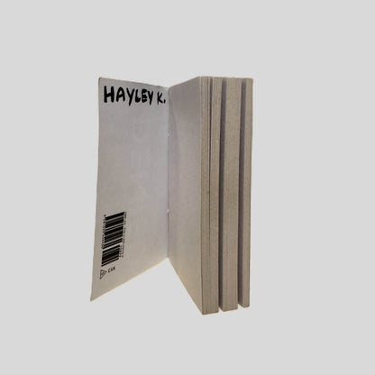 Inside front cover view of Denied by Mary Keliikoa centered on a neutral light gray background. The name "HAYLEY K." is written in black ink on the inside of the front cover. Pages are clean and crisp.