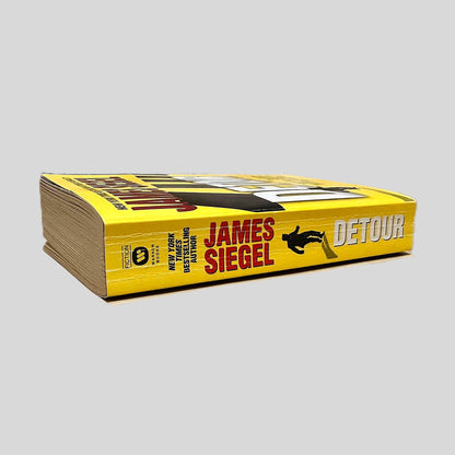 Close-up spine view of Detour by James Siegel centered on a neutral light gray background. Spine shows creasing. Some pages are dog-eared, but all pages lay flat.