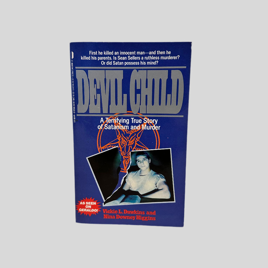Front cover view of The Devil Child by Dawkins and HIggins. Blue book cover with title in a silver font featuring a dark image of a boy in a torn photo with a pentagram behind it.