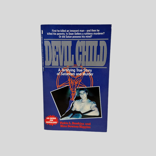 Front cover view of The Devil Child by Dawkins and HIggins. Blue book cover with title in a silver font featuring a dark image of a boy in a torn photo with a pentagram behind it.