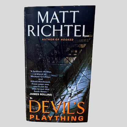 Front cover view of Devil's Plaything by Matt Richtel centered on a neutral light gray background. Creasing is present along the spine edge.