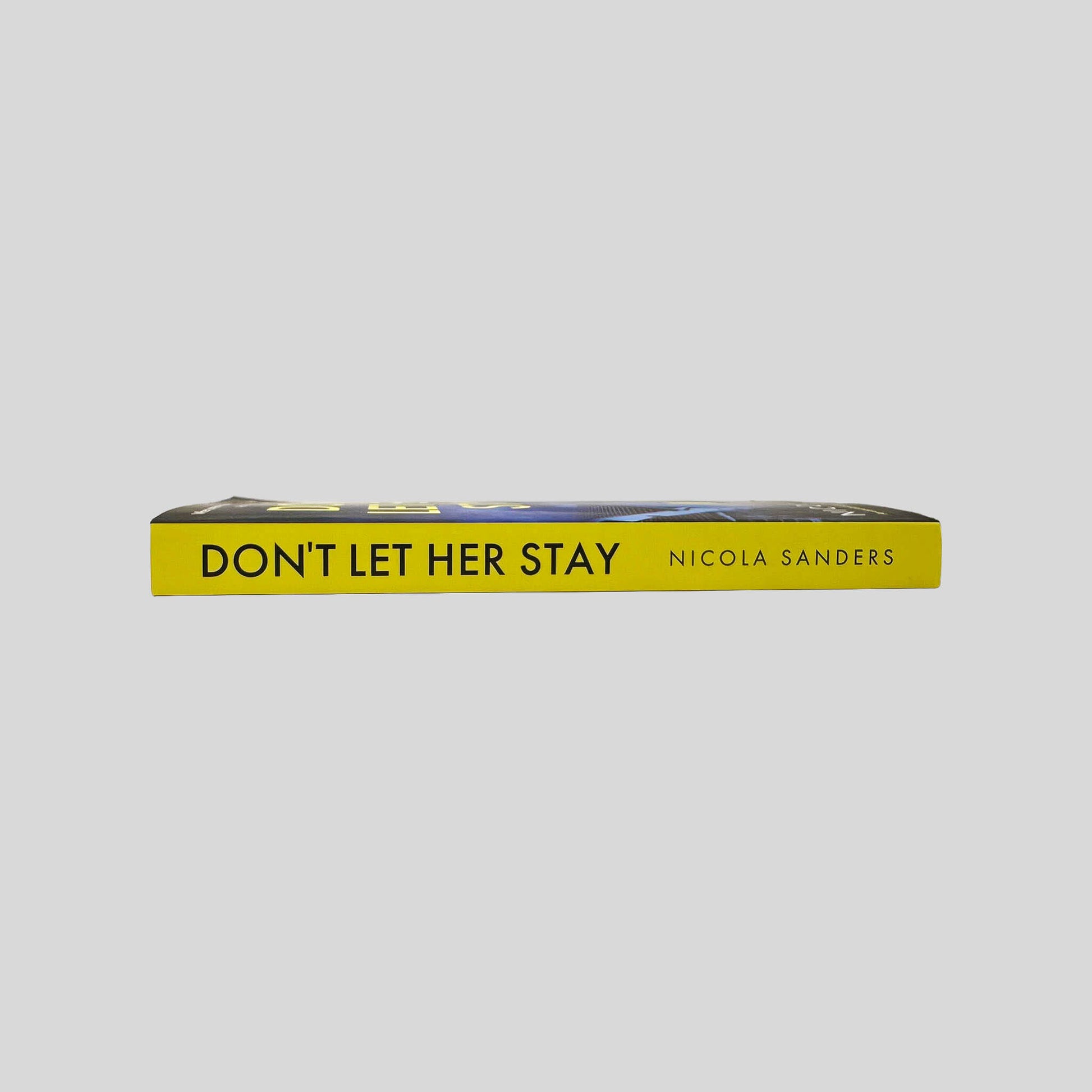 Close-up spine view of Don't Let Her Stay by Nicola Sanders centered on a neutral light gray background. Spine shows no creasing. Pages lay flat.