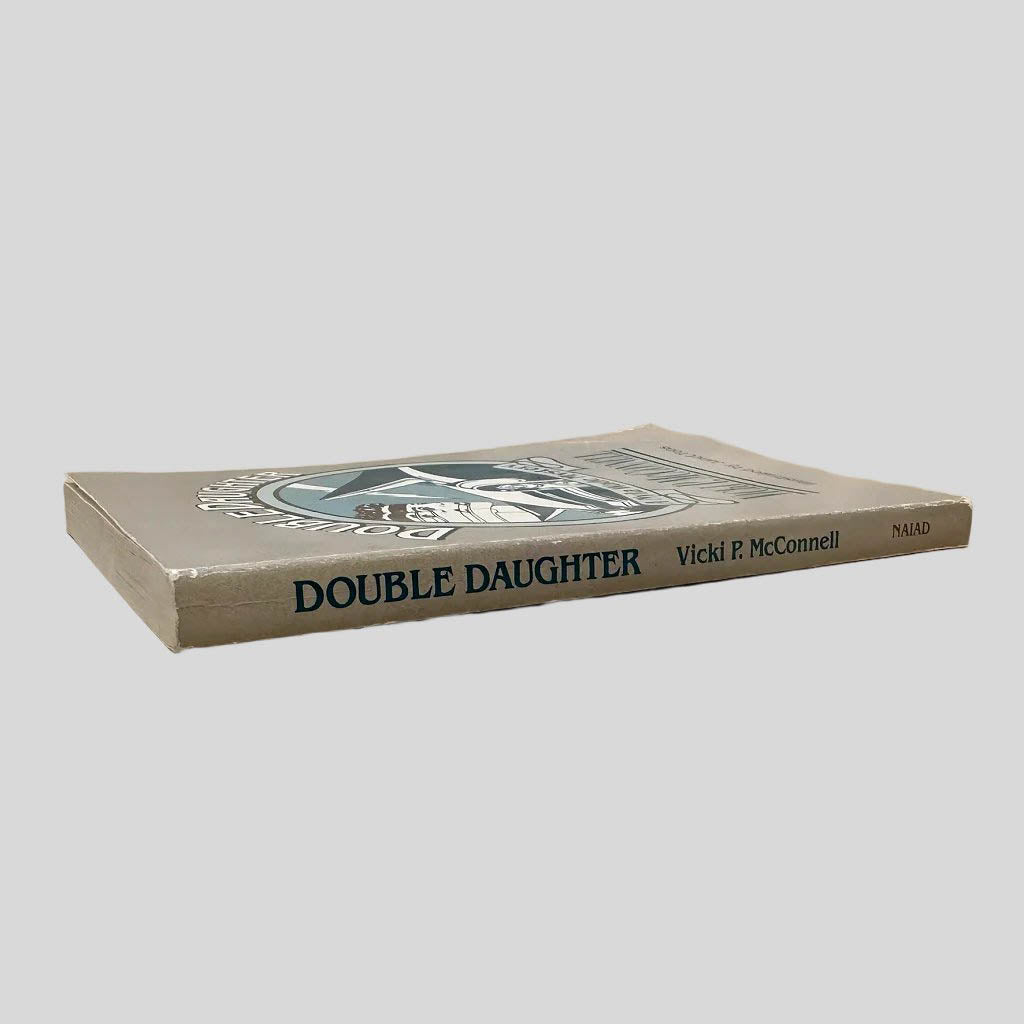 Close-up spine view of Double Daughter by Vicki P McConnell centered on a neutral light gray background. Spine is square and shows minimal creasing. Chipping is present at the top and bottom of spine. Pages lay flat.