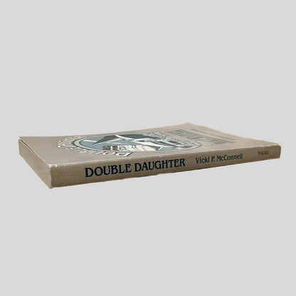 Close-up spine view of Double Daughter by Vicki P McConnell centered on a neutral light gray background. Spine is square and shows minimal creasing. Chipping is present at the top and bottom of spine. Pages lay flat.